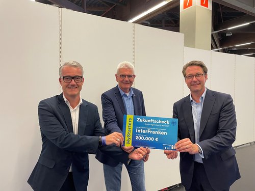 Bundesverkehrsminister Andreas Scheuer (r.) und der Bundestagsabgeordnete Artur Auernhammer (Mitte) übergeben den "Zukunftscheck" an InterFranken-Zweckverbandsvorsitzenden Patrick Ruh.